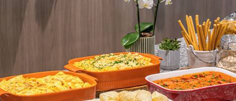 A buffet table with various dishes, including casseroles, bread rolls, and a dish with shredded carrots.