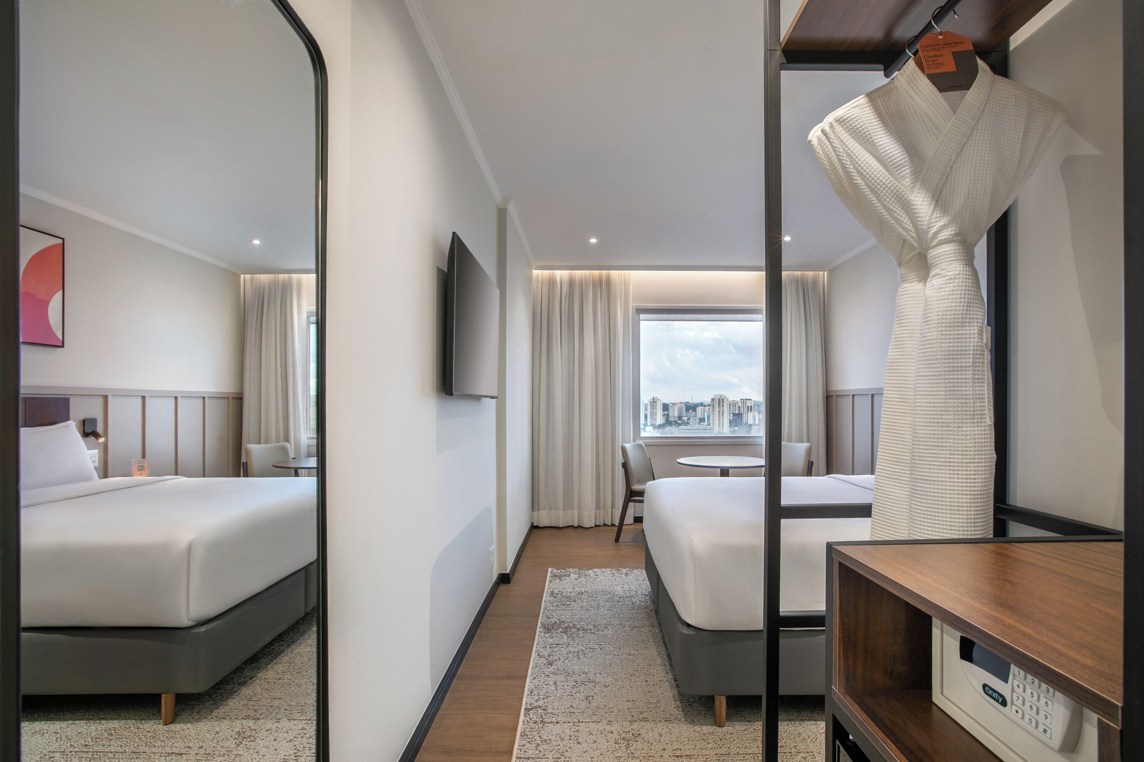 A hotel room with a bed, a desk, a chair, a TV, and a view of the city.