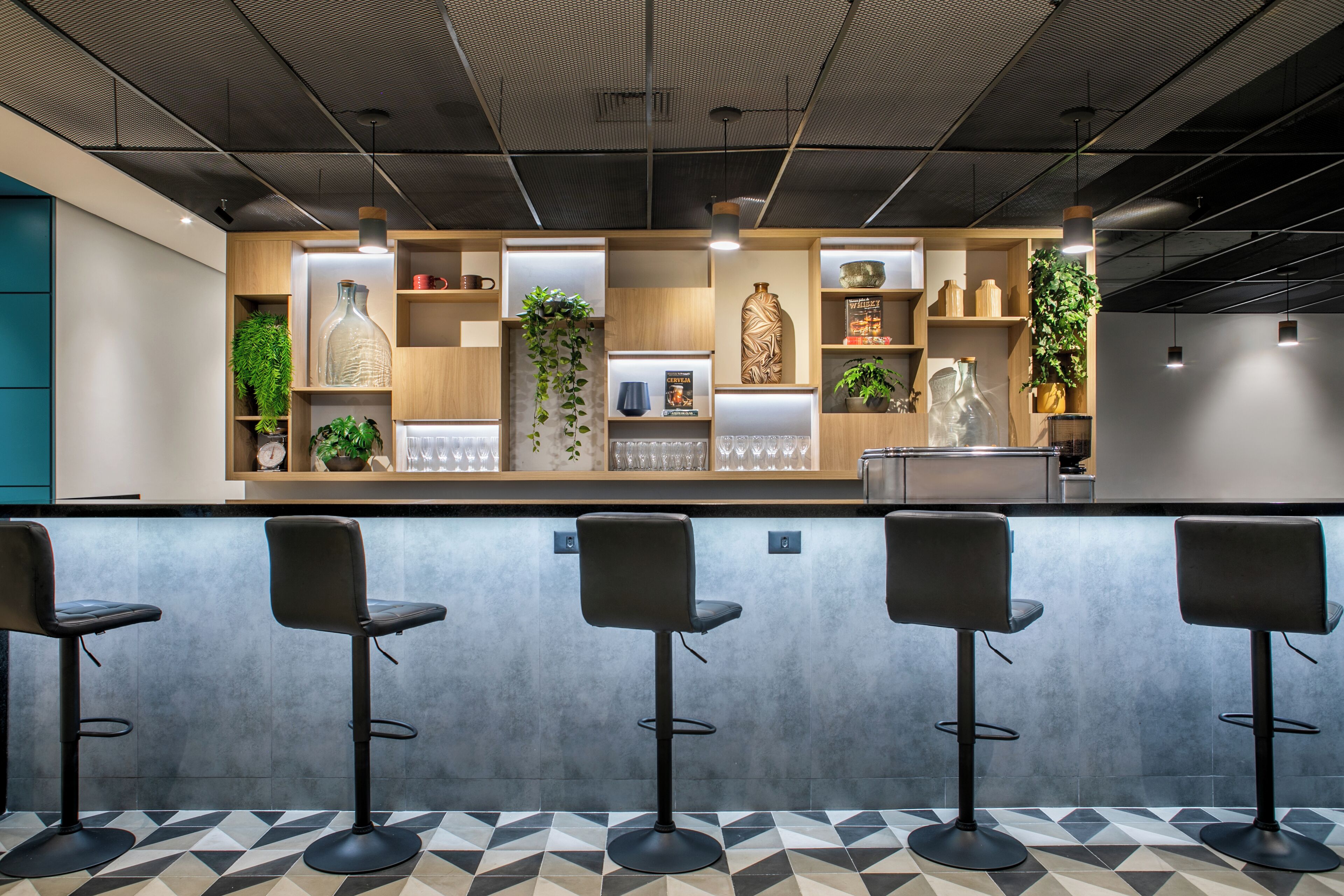 A modern bar area with a counter, bar stools, and shelves with decorative items and plants.