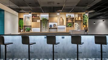 A modern bar area with a counter, bar stools, and shelves with decorative items and plants.