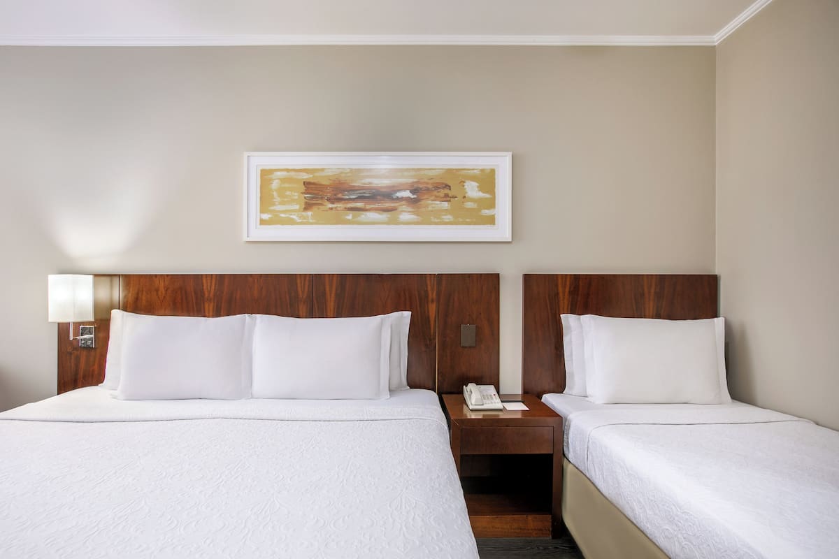 Ein Hotelzimmer mit zwei Betten, einem hölzernen Kopfteil, einem Nachttisch mit Telefon und einem gerahmten abstrakten Gemälde an der Wand.