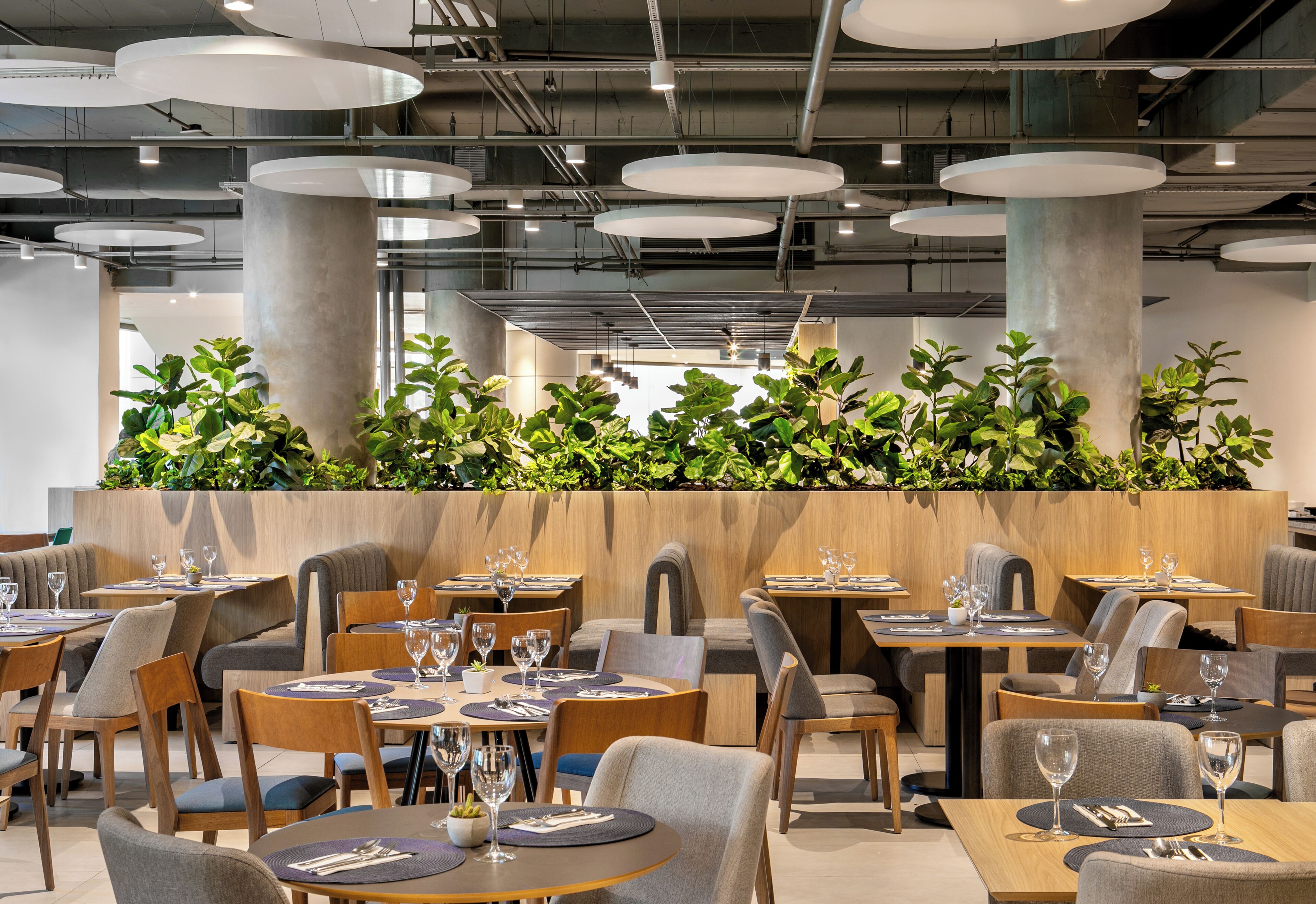 Un restaurante moderno con mesas redondas, asientos acolchados y una pared decorada con plantas verdes.