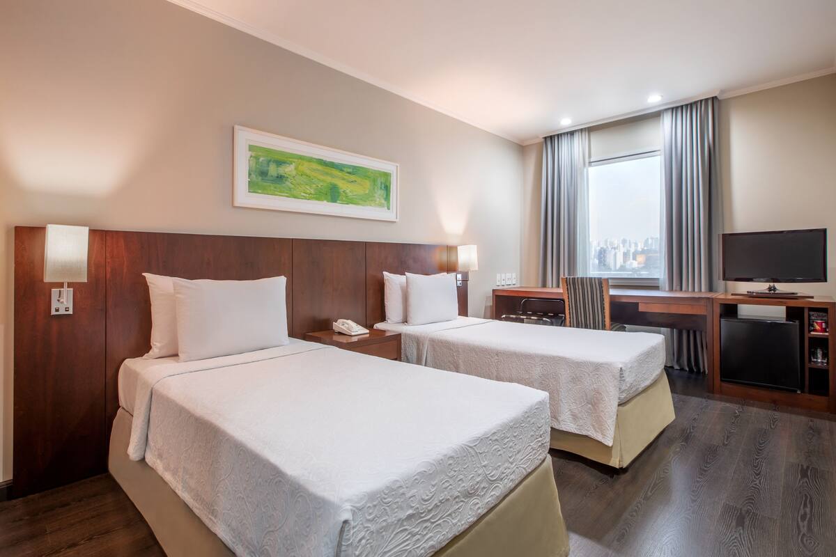 Ein Hotelzimmer mit zwei Betten, einem Schreibtisch, einem Fernseher und Blick auf die Stadt.