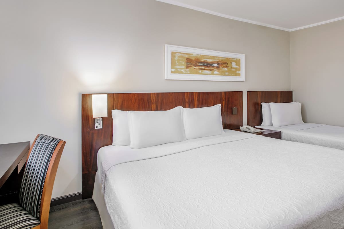 Ein Hotelzimmer mit zwei Betten, einem Schreibtisch, einem Sessel, einem Nachttisch und einer Wandlampe.