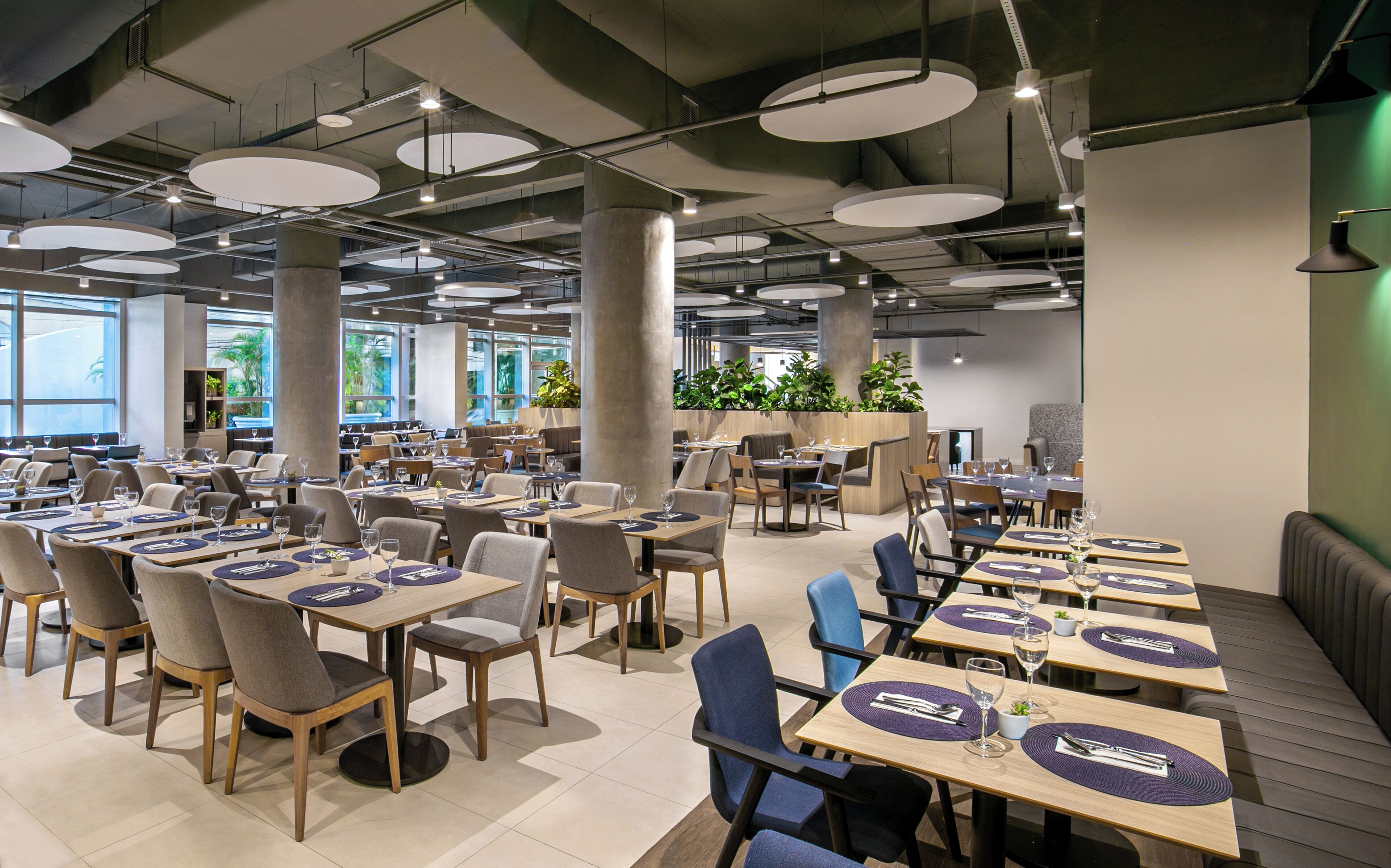 A modern restaurant with multiple dining tables and chairs, large windows, and hanging circular light fixtures.