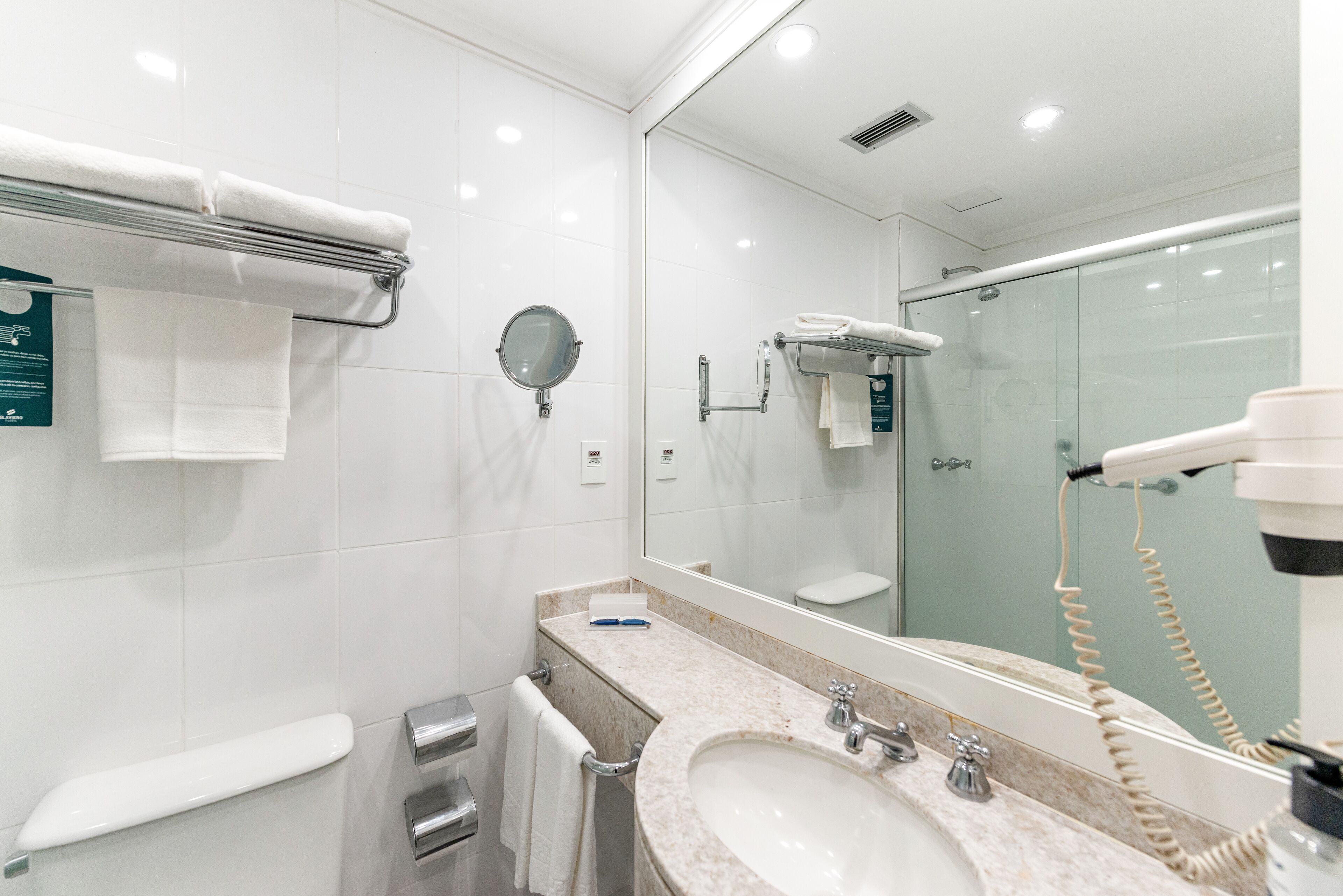 A modern bathroom with a large mirror, a sink, a towel rack, and a hairdryer.