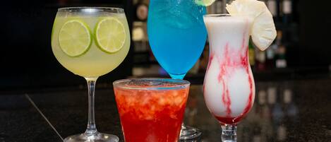 Four different cocktails on a bar counter with a blurred background of bottles.