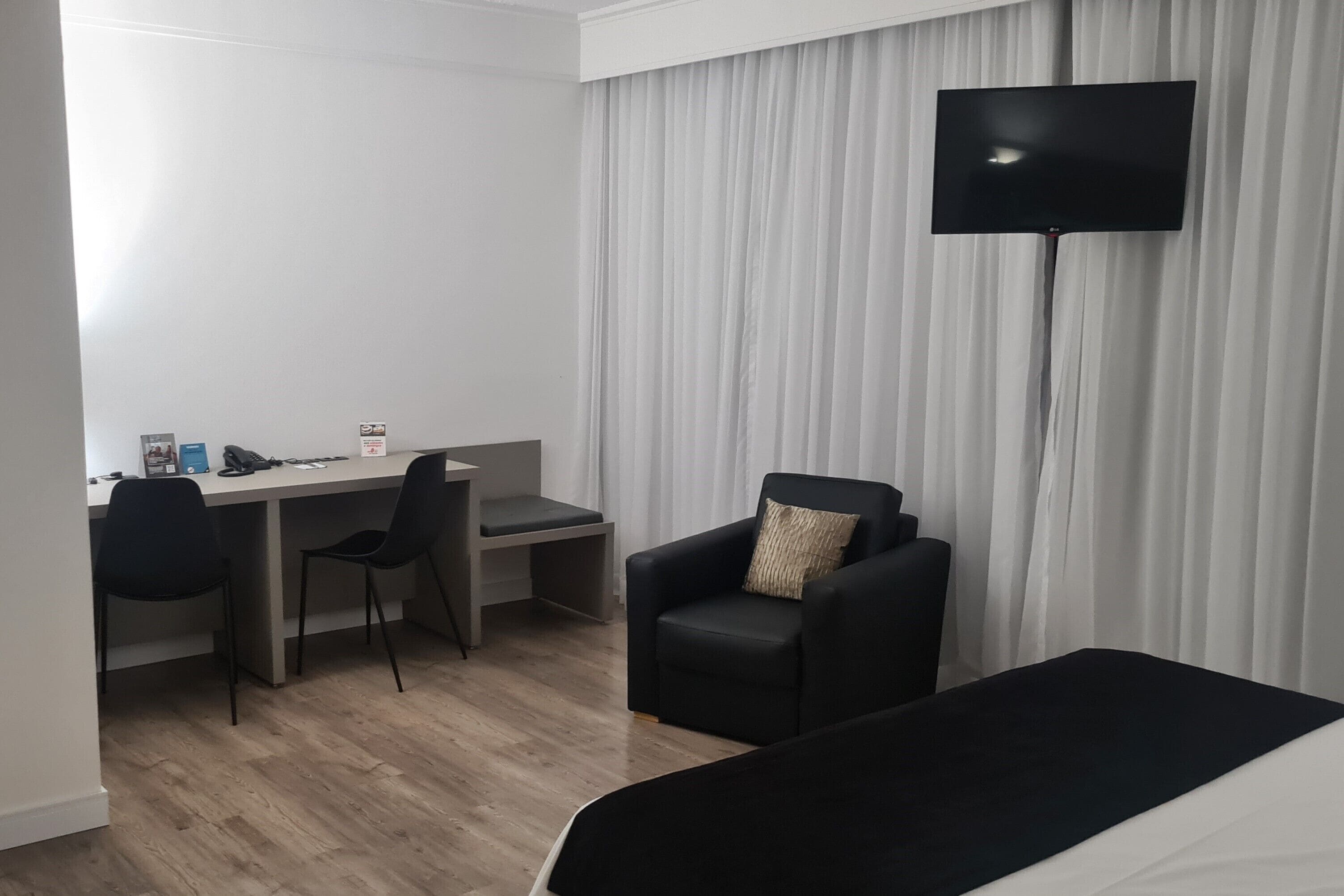 Ein Hotelzimmer mit einem Bett, einem Schreibtisch, zwei Stühlen, einem Fernseher und einem Vorhang.