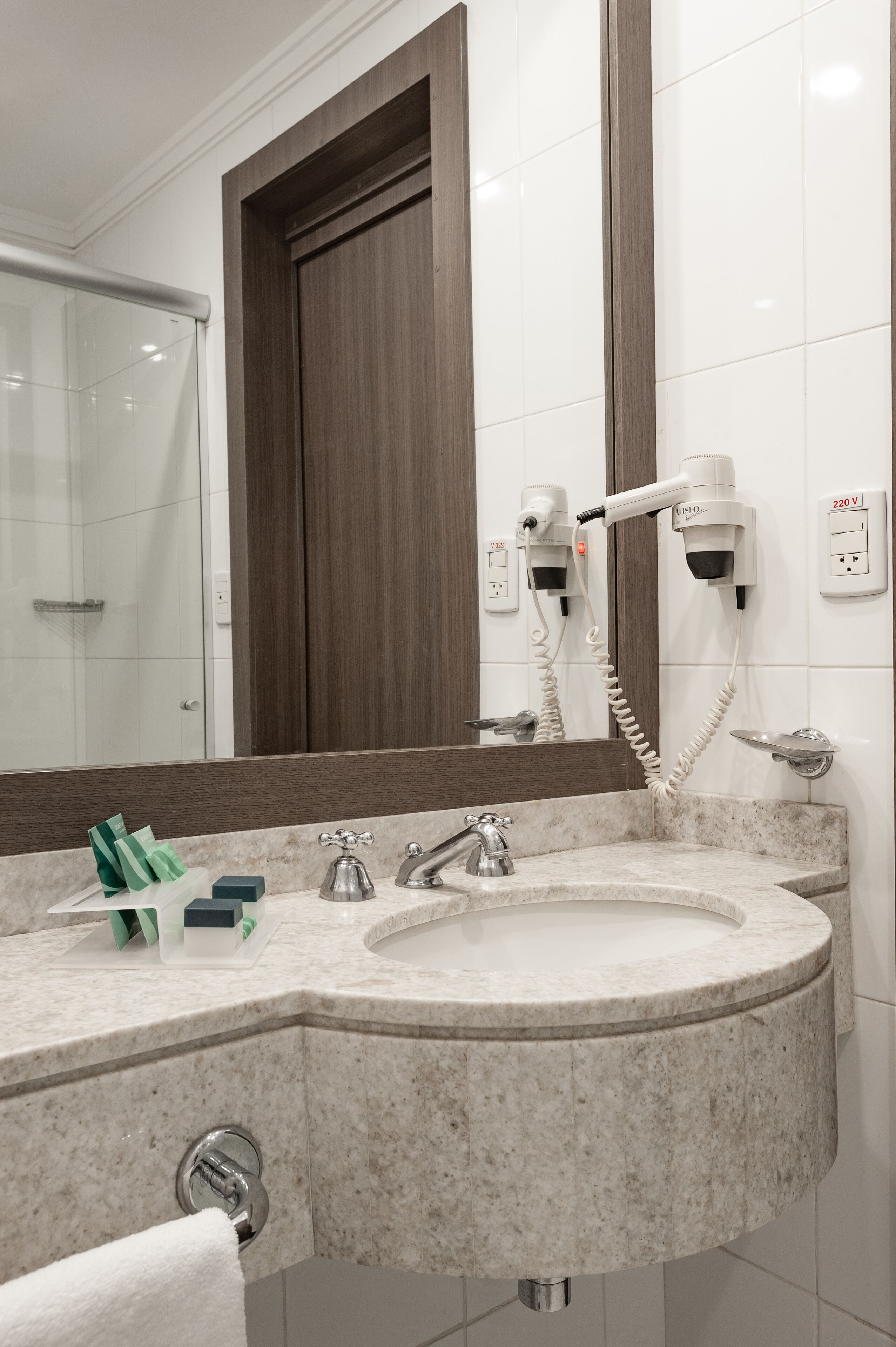 Uma casa de banho com uma sanita dupla, um espelho, um secador de cabelo e um porta-toalhas.