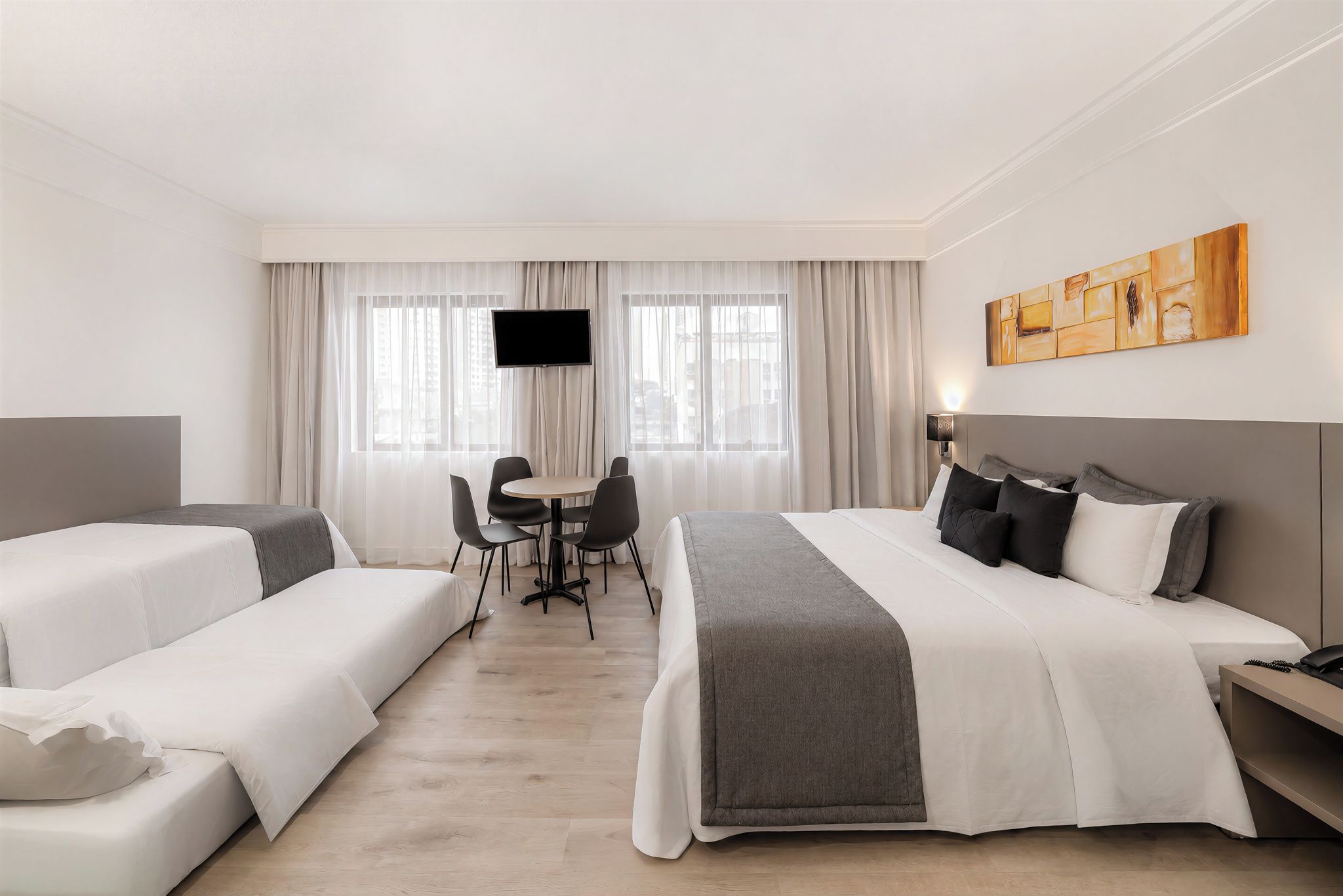 A hotel room with two beds, a desk, chairs, a TV, and a painting on the wall.