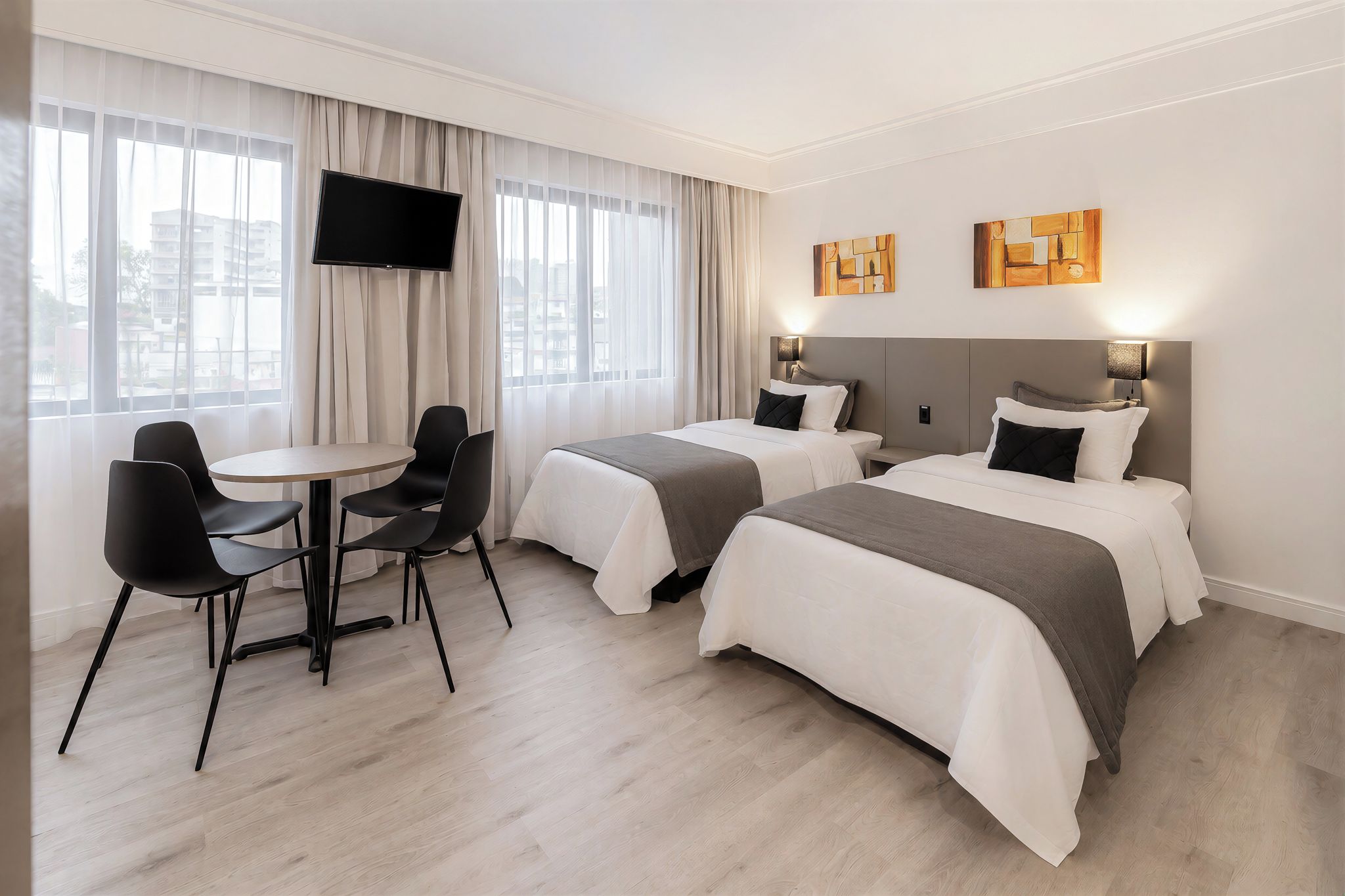 Hotellihuone, jossa on kaksi sänkyä, televisio, työpöytä tuoleineen ja taideteoksia seinällä.