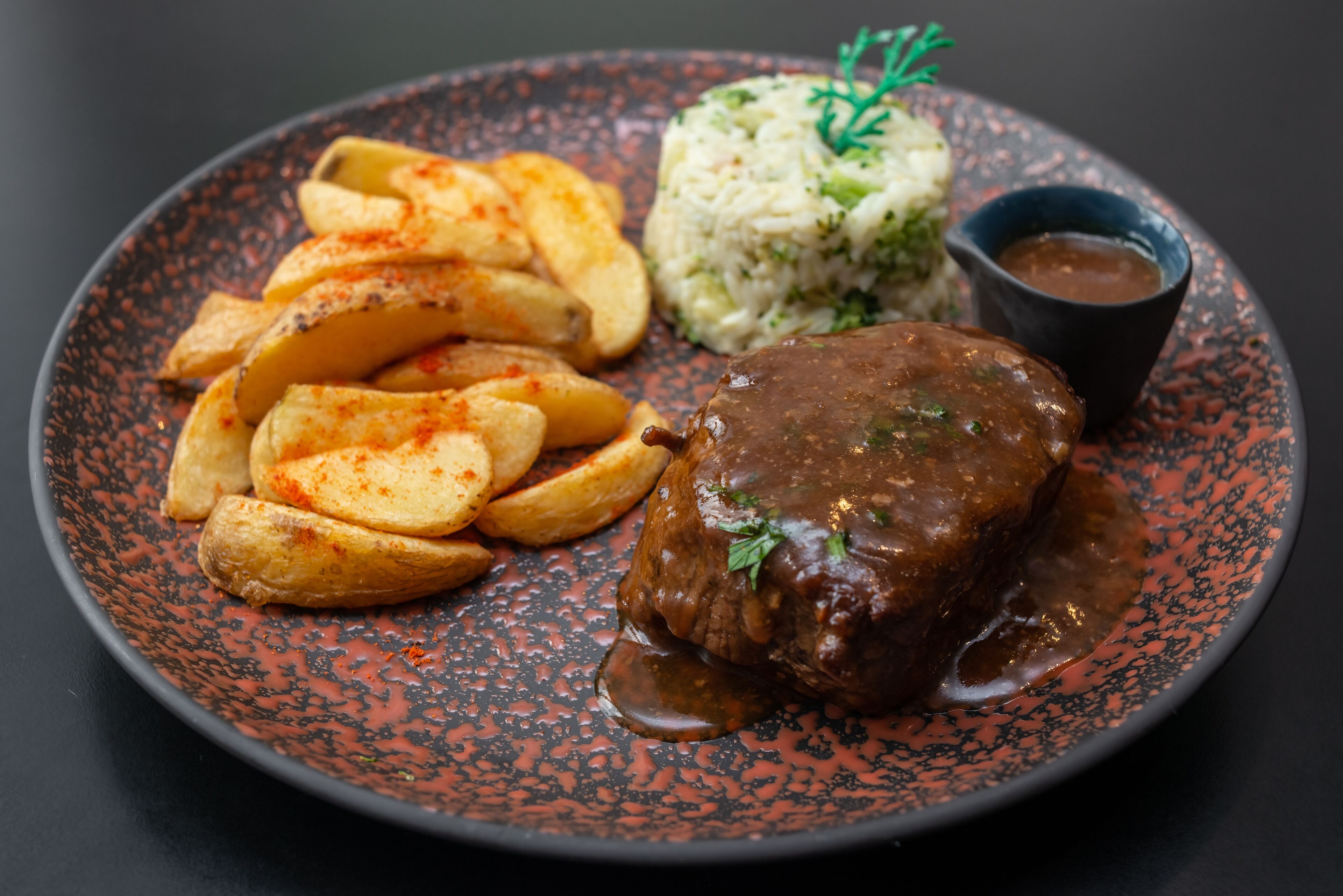 A plate with a meat dish, potato wedges, rice, and a sauce.