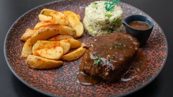 A plate with a meat dish, potato wedges, rice, and a sauce.