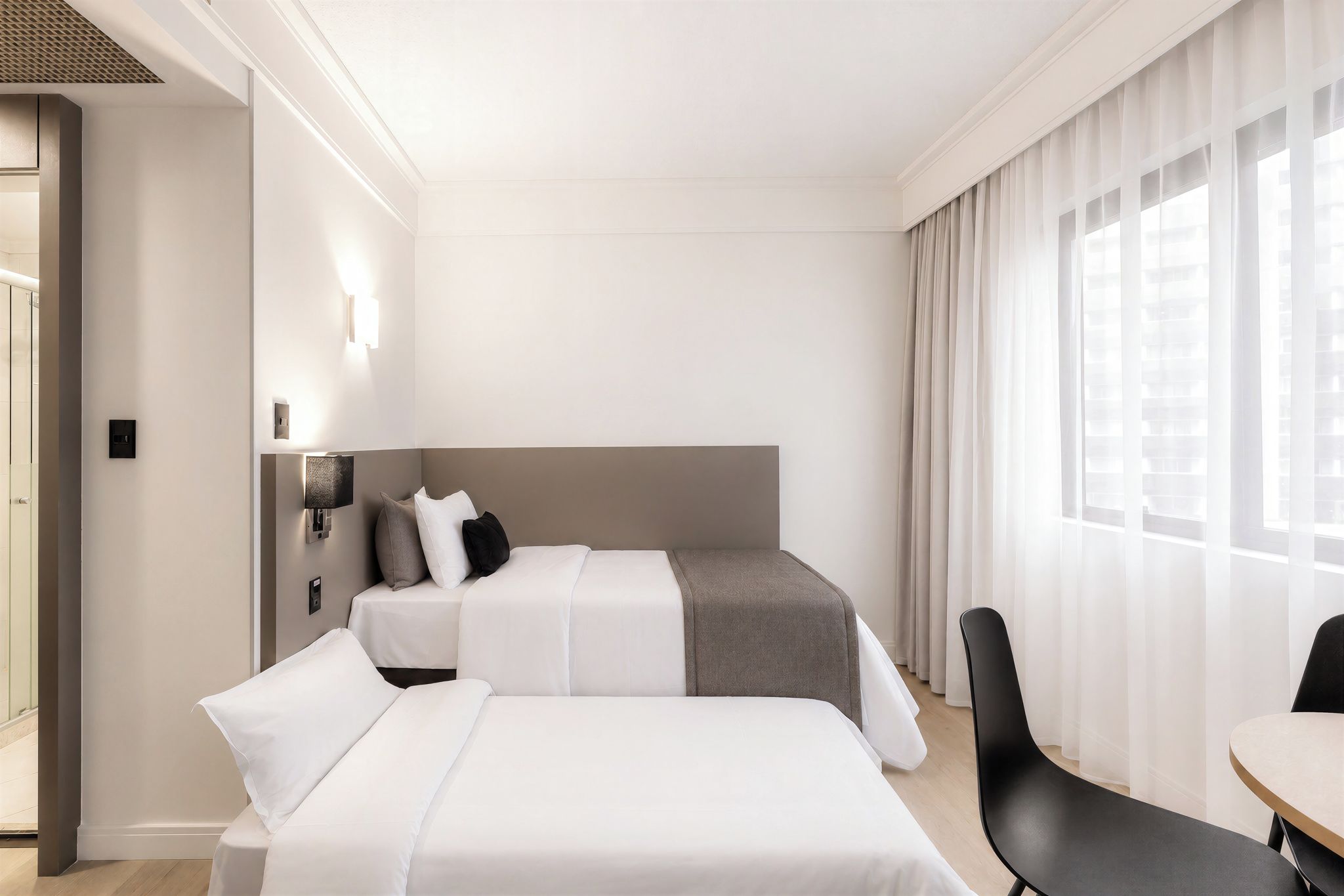 A hotel room with two beds, a desk, and a chair.