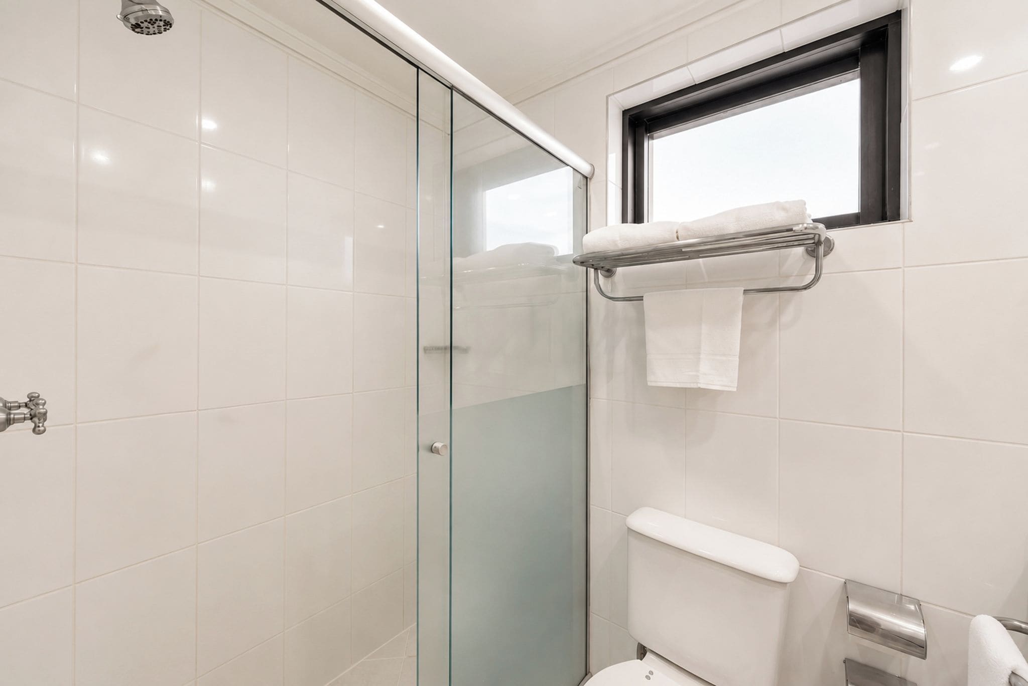 A modern bathroom with a glass shower enclosure, a toilet, and a towel rack.