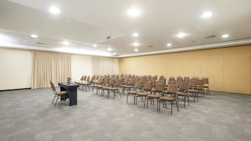 A conference room with rows of chairs, a table with a laptop, and a carpeted floor.