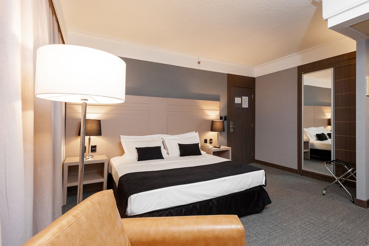 A hotel room with a large bed, bedside tables, a lamp, a mirror, and a chair.