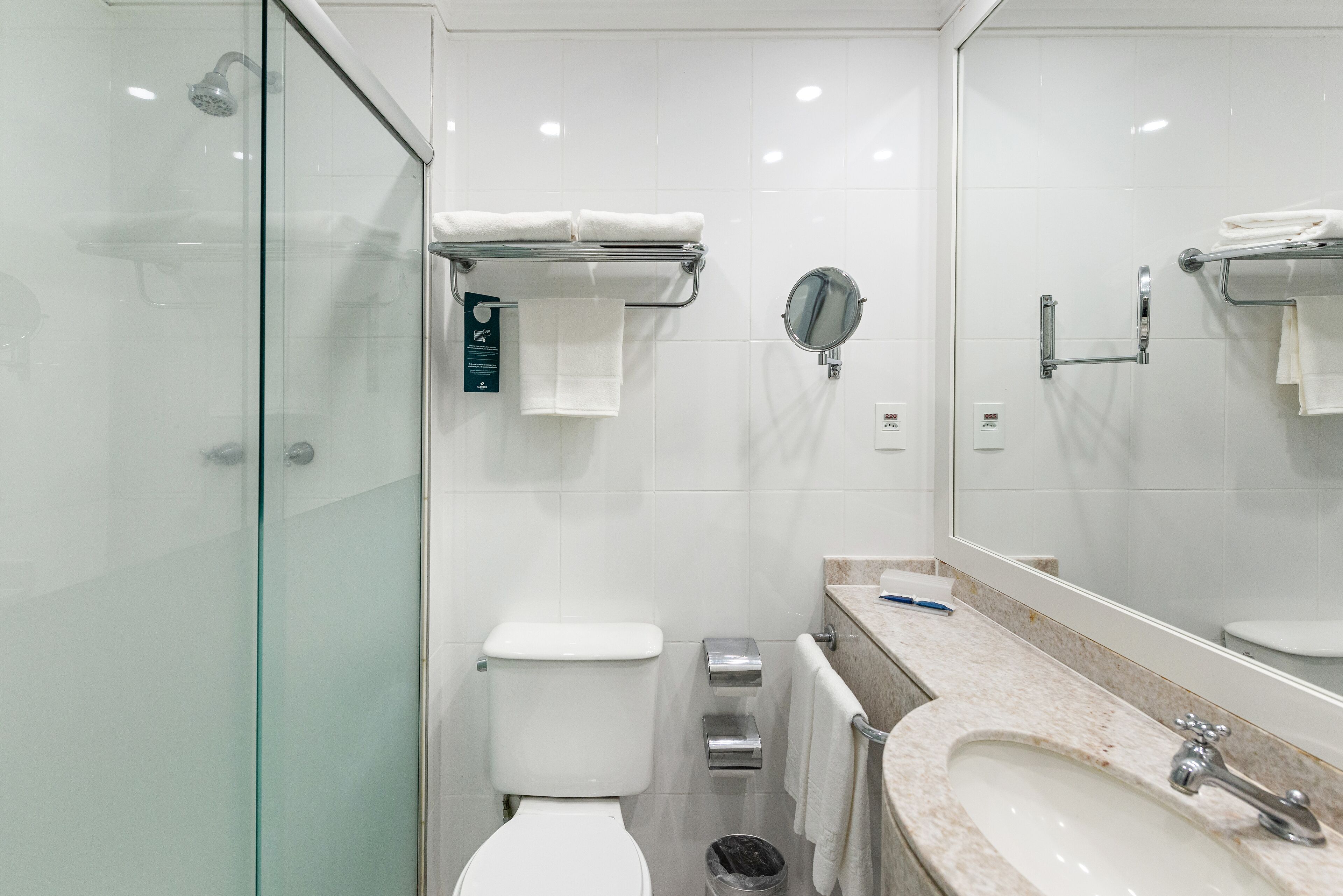 A modern bathroom with a glass shower enclosure, a toilet, a bidet, a sink with a mirror, and a towel rack.