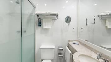 A modern bathroom with a glass shower enclosure, a toilet, a bidet, a sink with a mirror, and a towel rack.