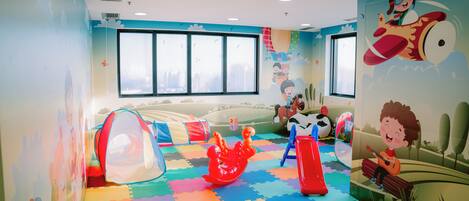 Una sala de juegos infantil con tapetes de espuma de colores, un tobogán y una tienda de campaña.
