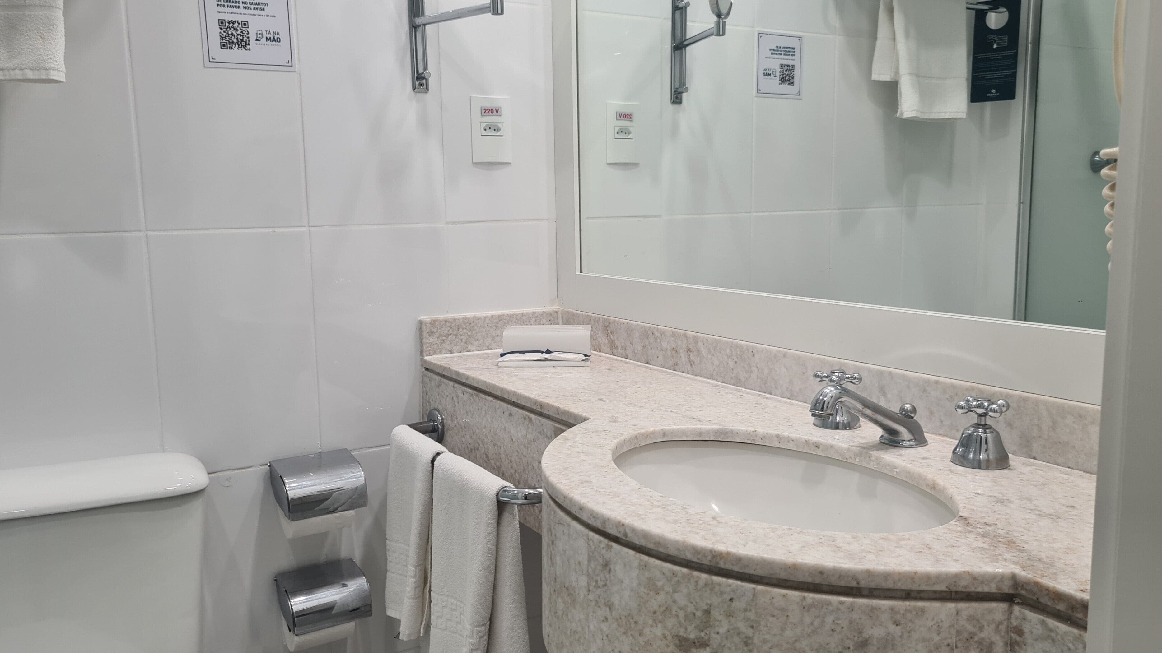 Un baño con lavamanos de mármol, un espejo y un dispensador de toallas.