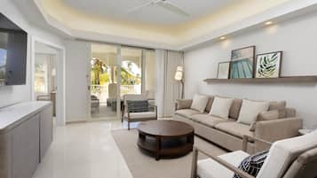 A modern living room with a sofa, armchairs, a coffee table, and a TV. There is a sliding glass door leading to an outdoor area with a balcony.