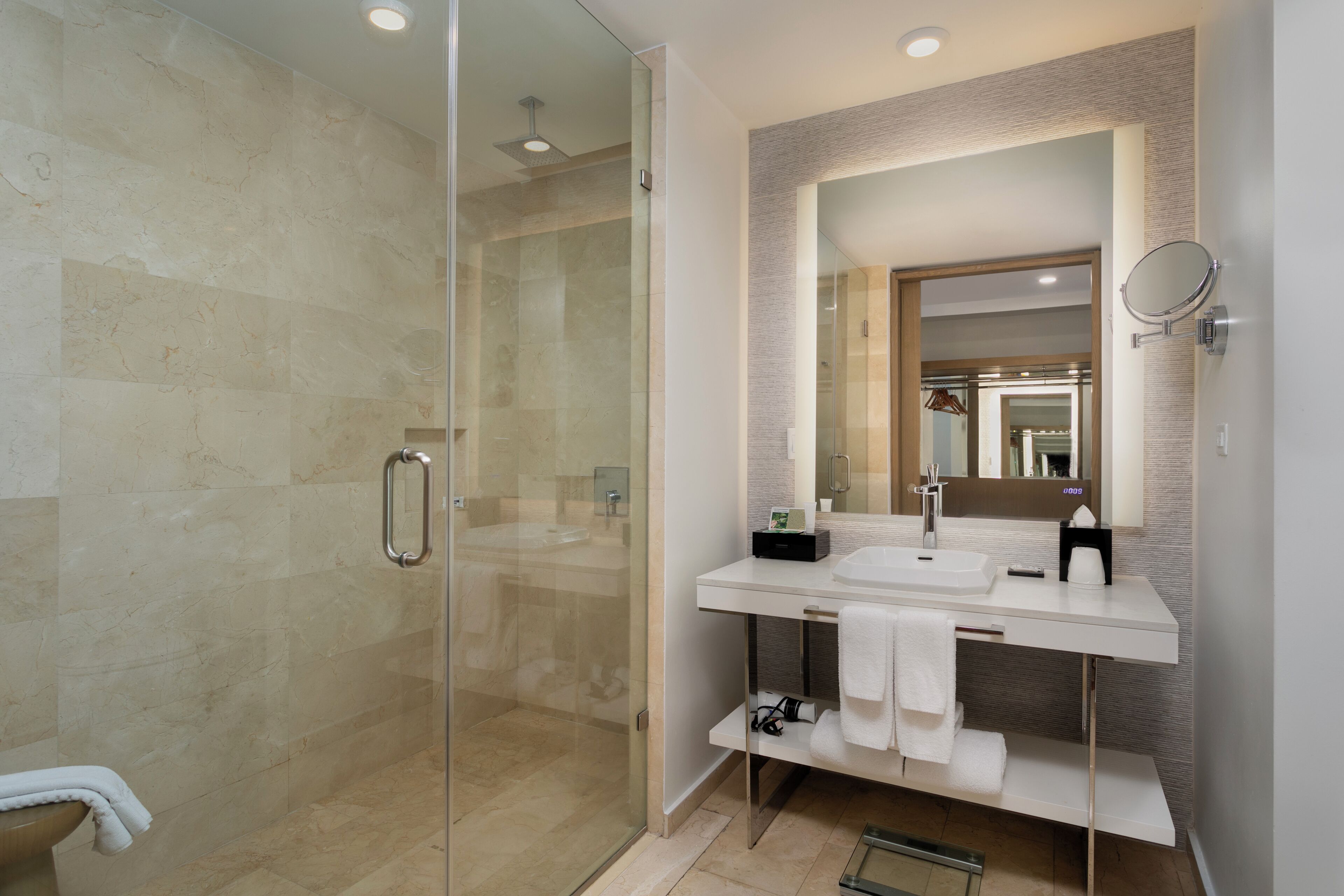 Un baño moderno con ducha envuelta en vidrio, tocador blanco con un espejo grande y un perchero para toallas.