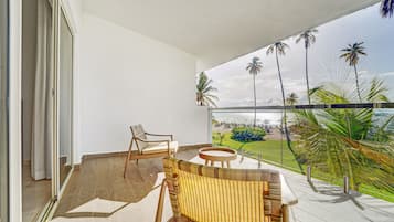 A balcony with a wicker sofa, a wooden chair, and a small table.