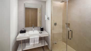 Un baño moderno con ducha envuelta en cristal, un lavamanos blanco y un espejo encima.