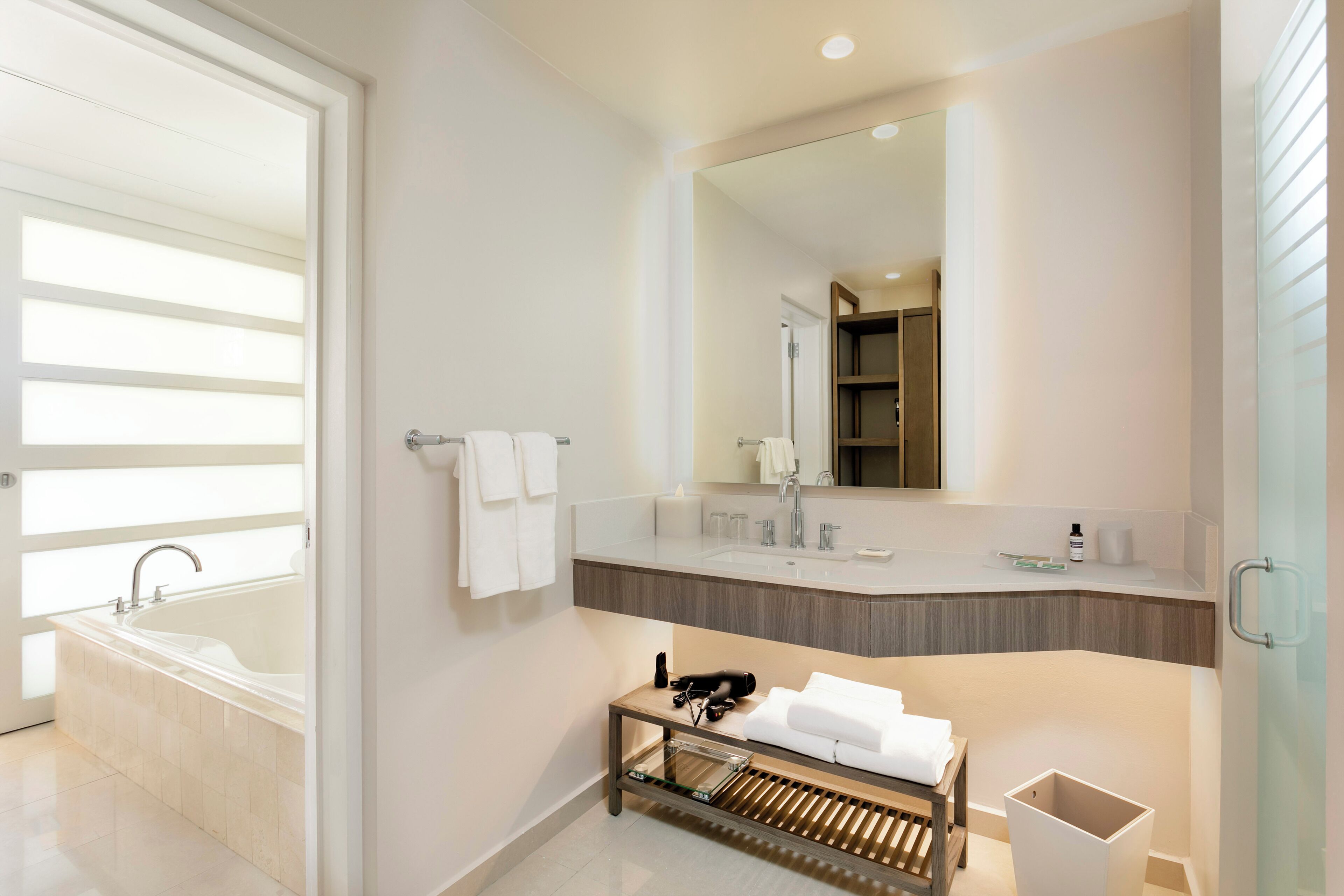 A modern bathroom with a large bathtub, a vanity with a mirror, and a wooden bench.