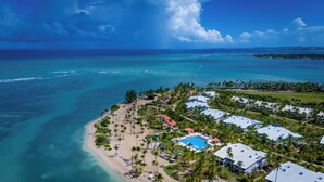 An aerial view of a coastal resort with a beach, pool, and multiple buildings.