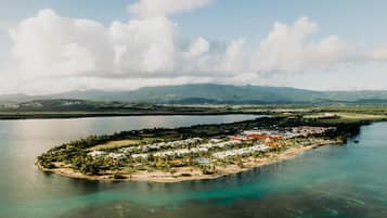 An aerial view of a small island with a resort area, surrounded by water and mountains in the background.