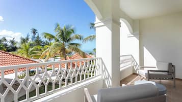 A balcony with a view of the ocean and palm trees, white railings, and a seating area with a table and chairs.