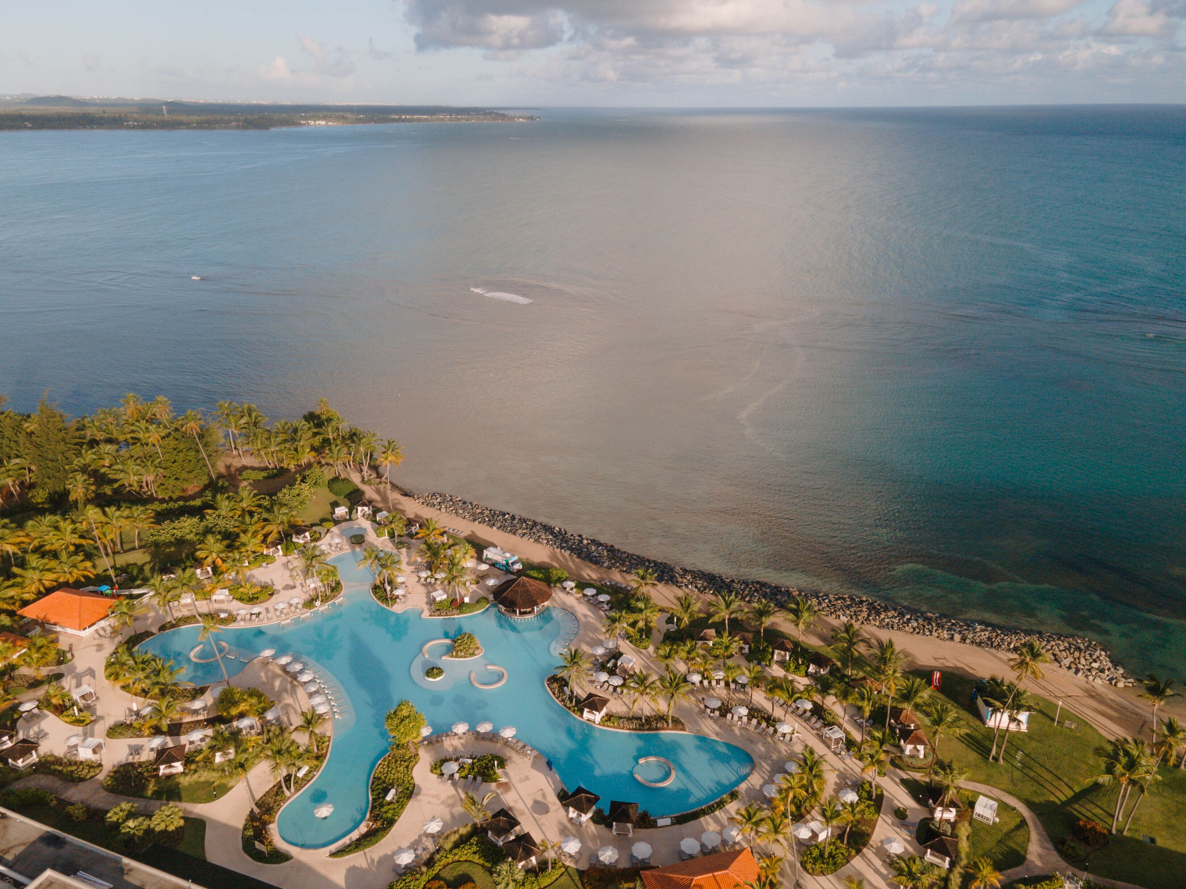 Vue aérienne d’un complexe hôtelier doté d’une grande piscine, de palmiers et d’une plage.