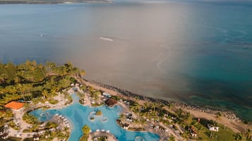 Vue aérienne d’un complexe hôtelier doté d’une grande piscine, de palmiers et d’une plage.