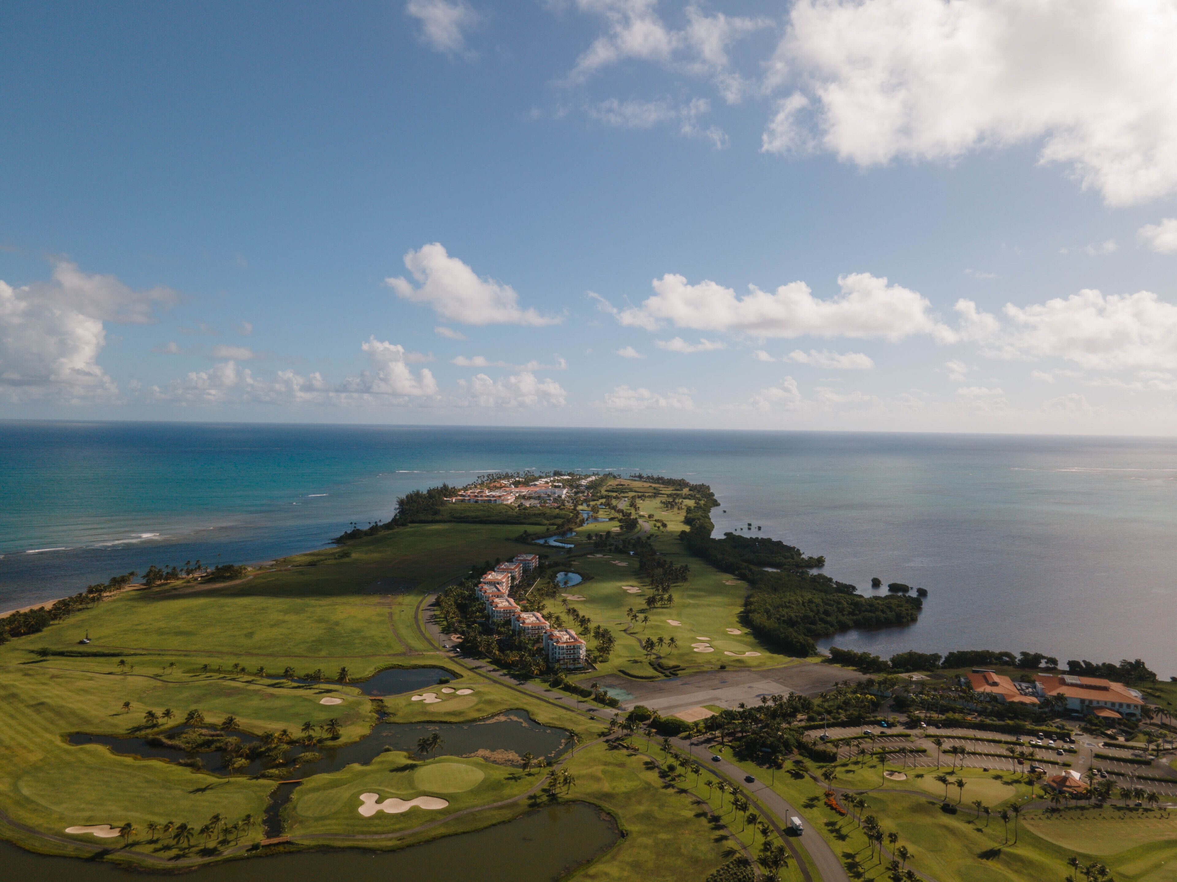 An aerial view of a golf course with a large body of water, a clubhouse, and surrounding greenery.