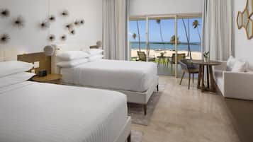 A hotel room with two beds, a balcony with a view of the beach, and a seating area with a table and chairs.