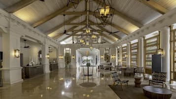 A spacious lobby with high ceilings, wooden beams, and a polished floor. There are seating areas with chairs and tables, and a reception desk with a counter.