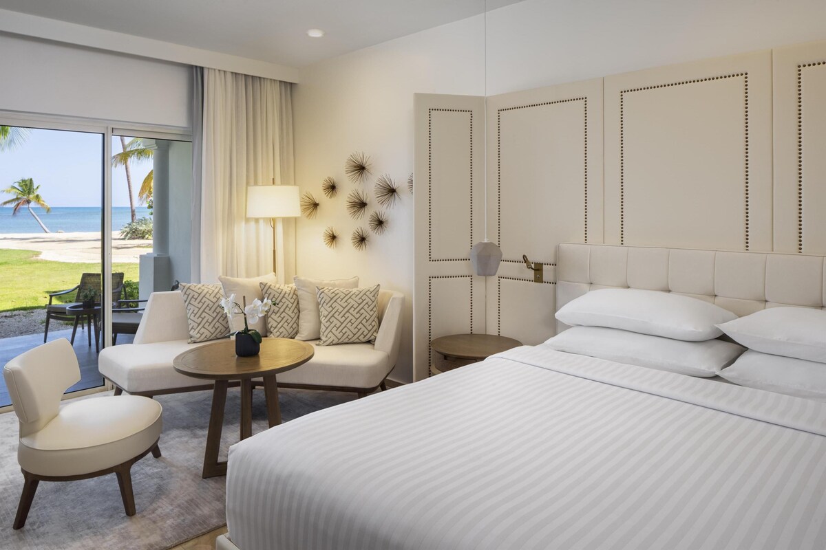 Une chambre d’hôtel avec un grand lit, un coin salon avec une table et une vue sur la plage.