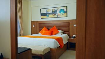 Habitación de hotel con cabecera de madera, cama con ropa de cama naranja, mesita de noche y escritorio con silla.
