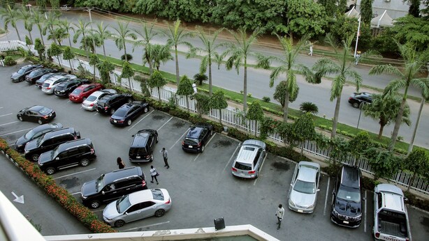 A parking lot with multiple cars and a pedestrian walking. - Stratton Hotel Asokoro (Abuja)