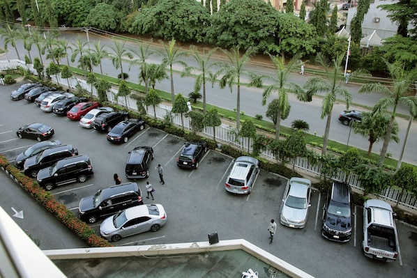 A parking lot with multiple cars and a pedestrian walking. - Stratton Hotel Asokoro (Abuja)