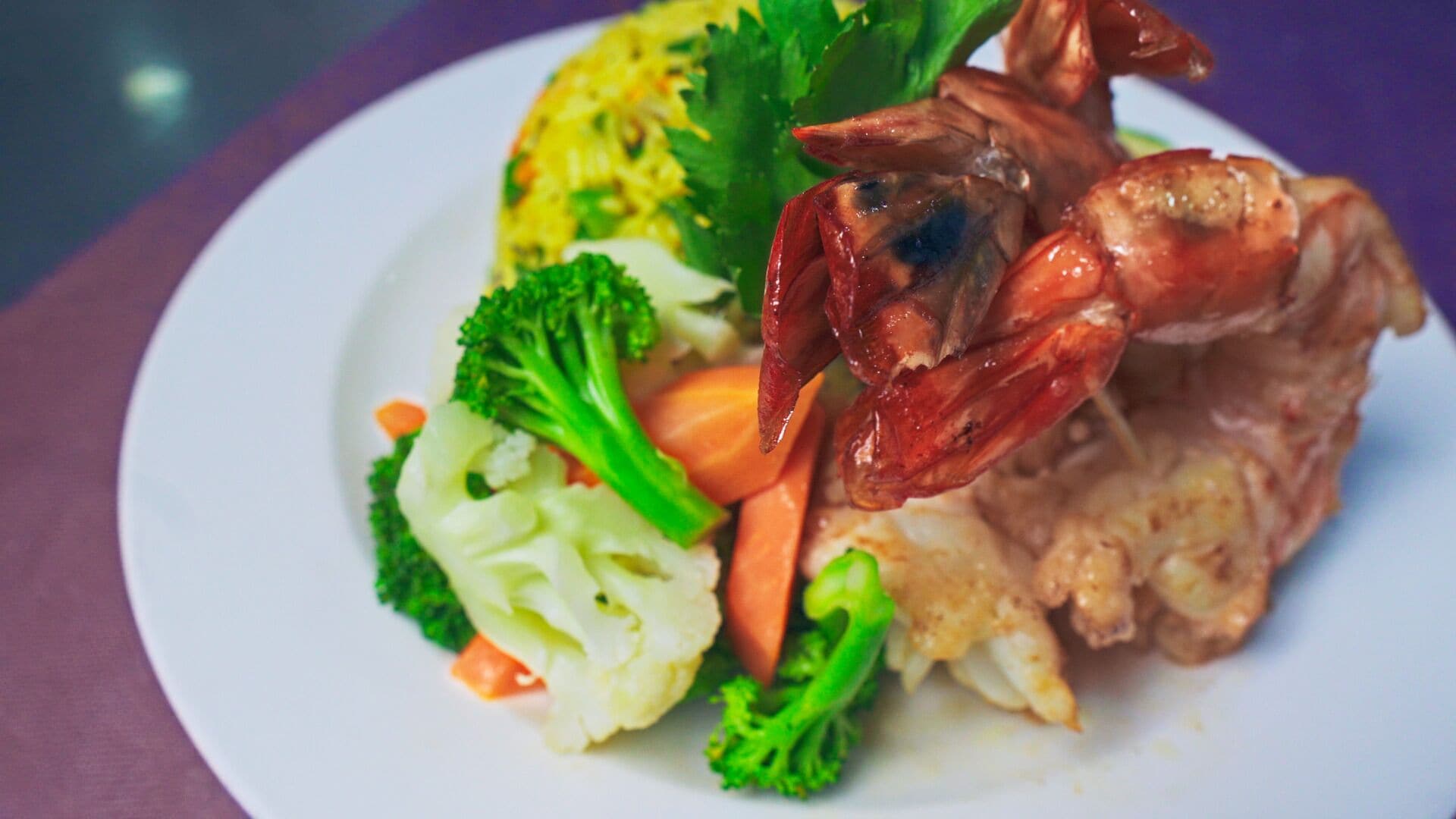 A plate with a lobster tail, broccoli, cauliflower, and a side of rice.