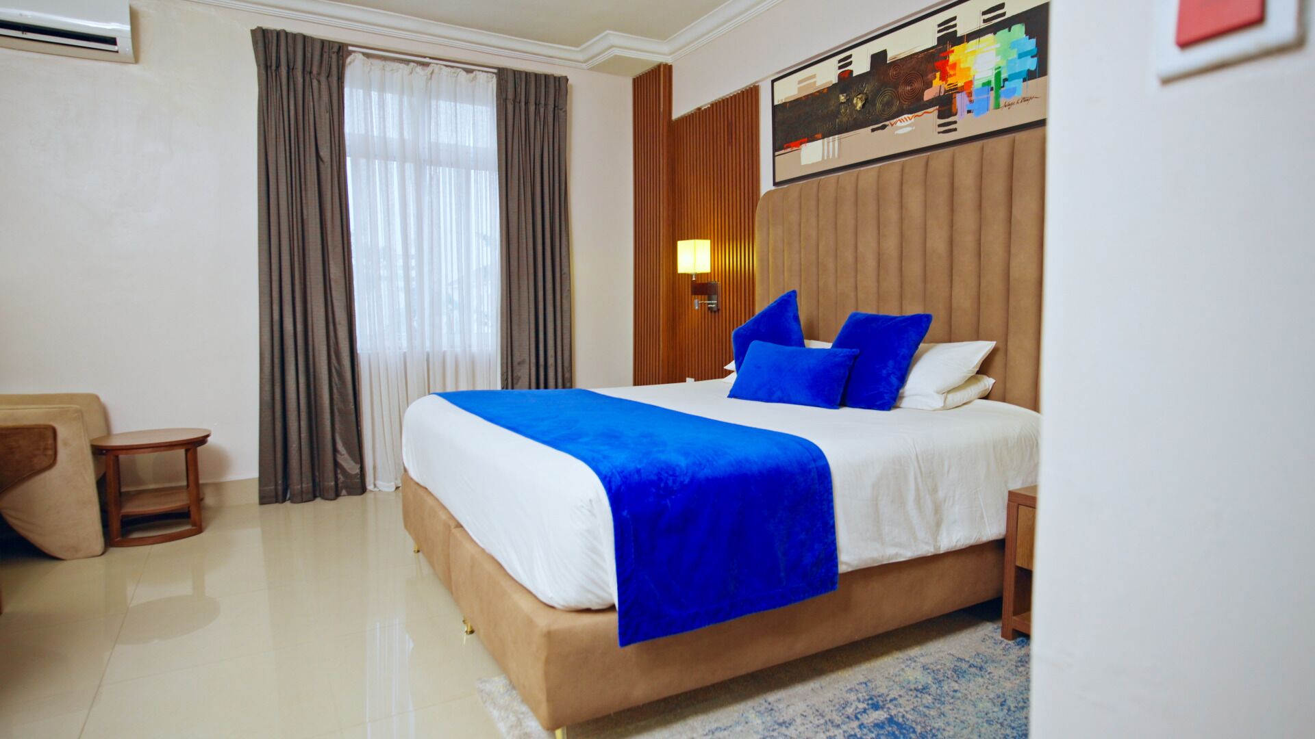 A hotel room with a large bed, a nightstand, a lamp, and a painting on the wall.