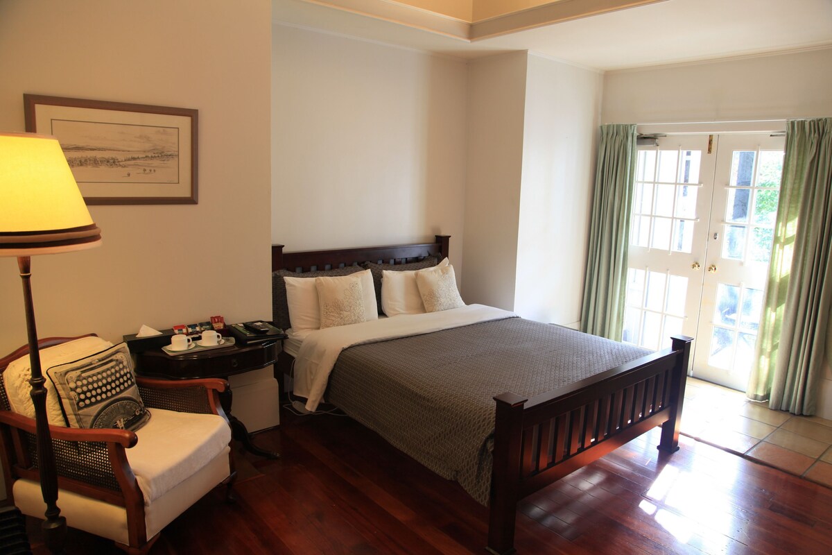 A neatly arranged bedroom with a bed, a chair, a nightstand, a lamp, and a window with curtains.