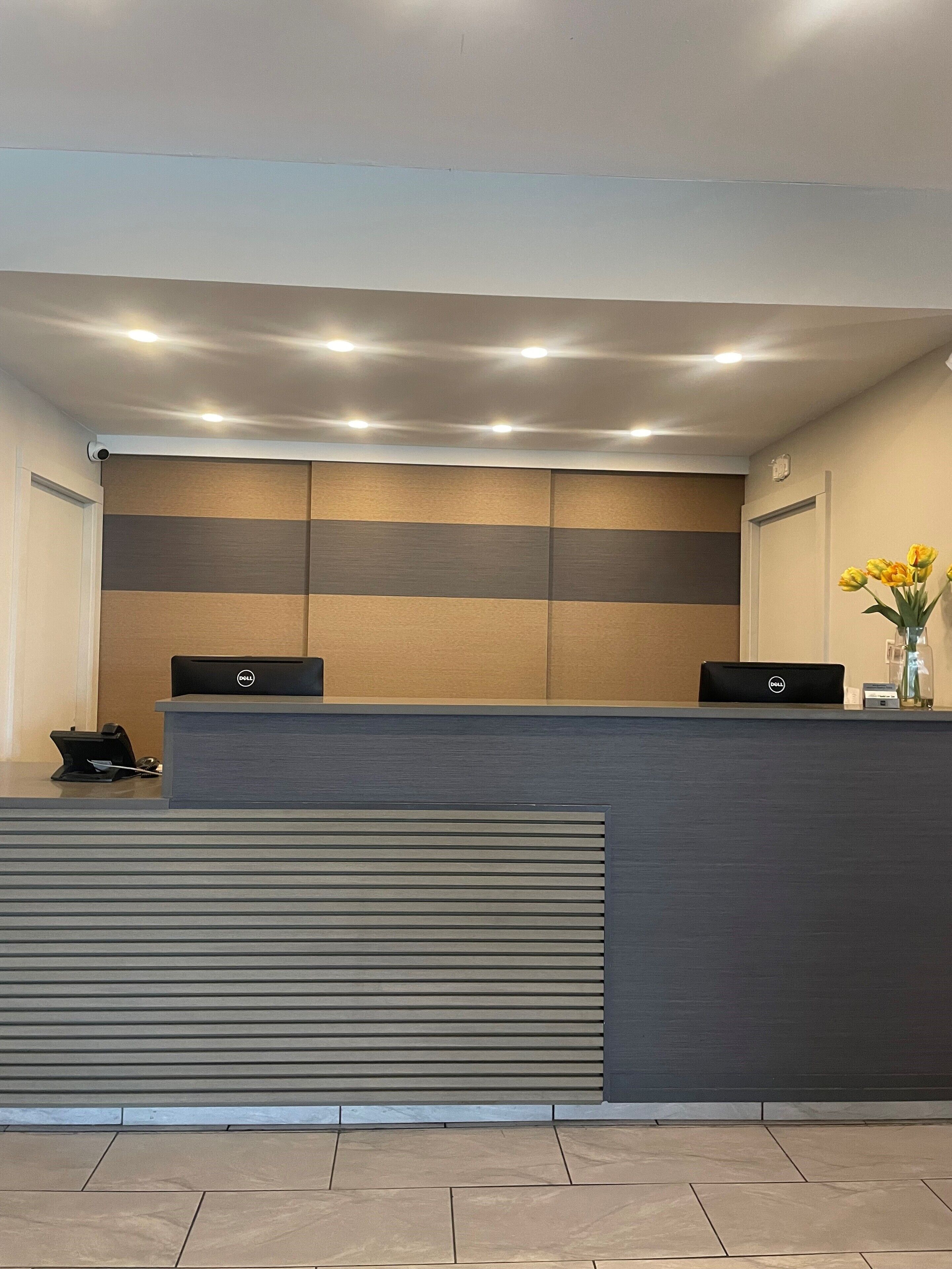 A reception desk with two Dell computers, a vase with yellow flowers, and a security camera on the wall.
