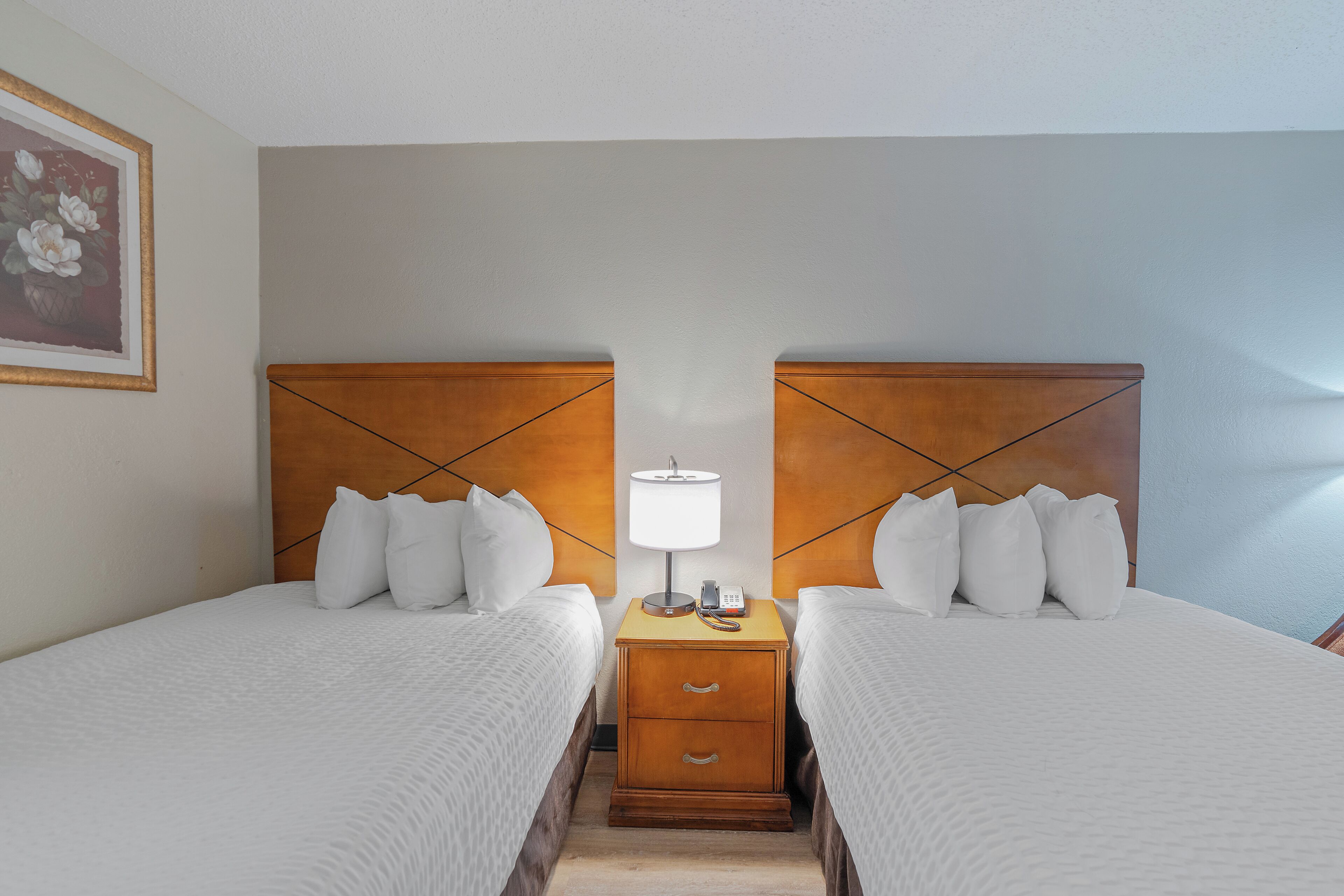 A hotel room with two beds, a nightstand with a lamp, and a framed picture on the wall.