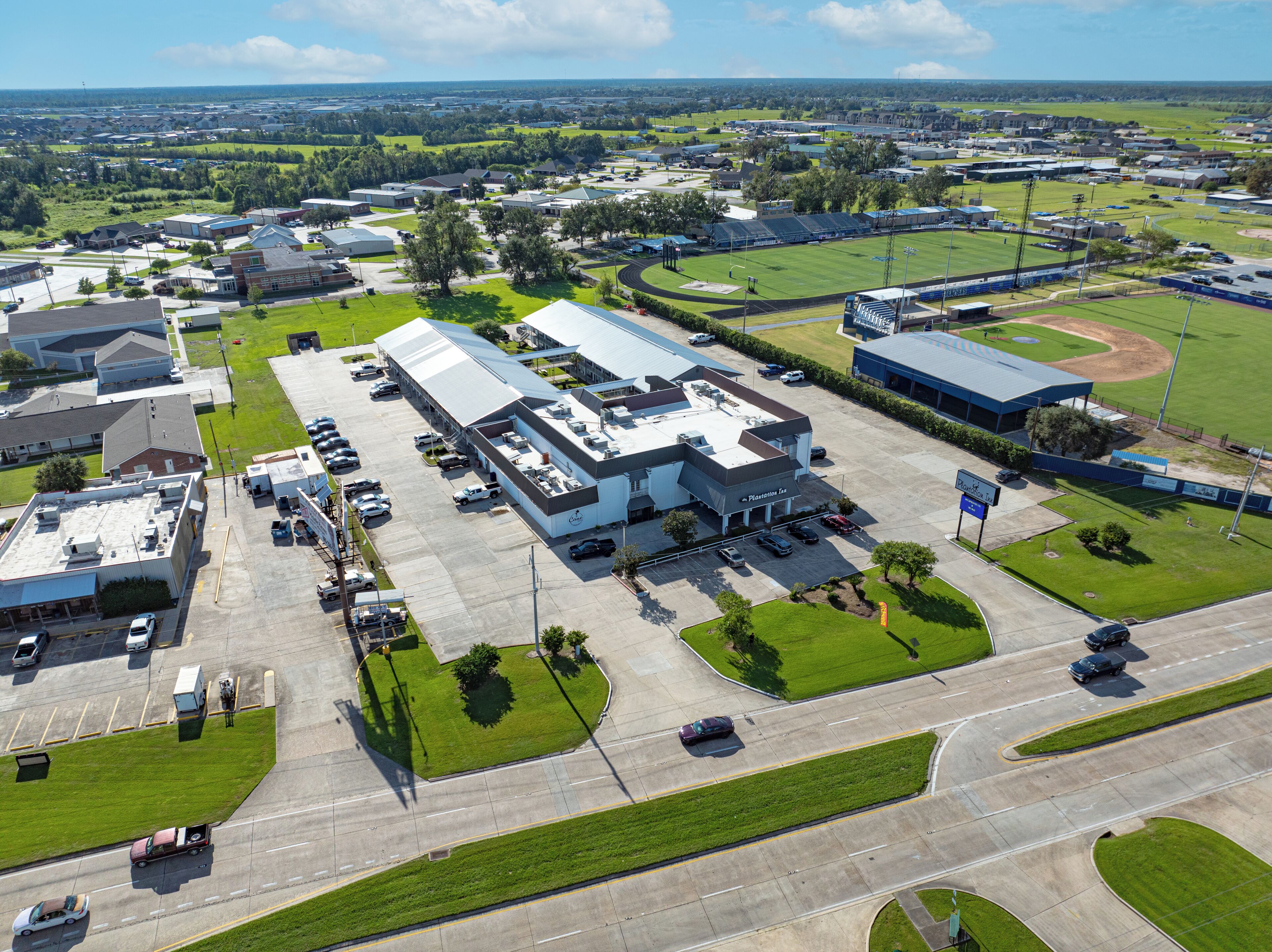 Vue aérienne d’un immeuble commercial, avec un parking, des espaces verts adjacents et un terrain de baseball.