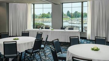A conference room with a round table and chairs, large windows with a view of a river and bridge, and a balcony with a railing.