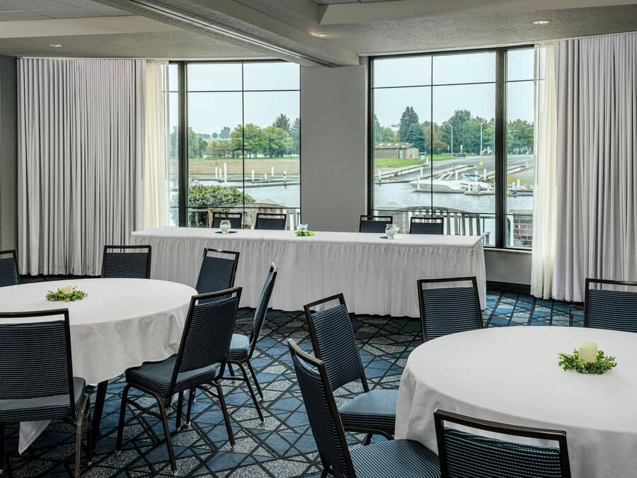A conference room with a round table and chairs, large windows with a view of a river and bridge, and a balcony with a railing.